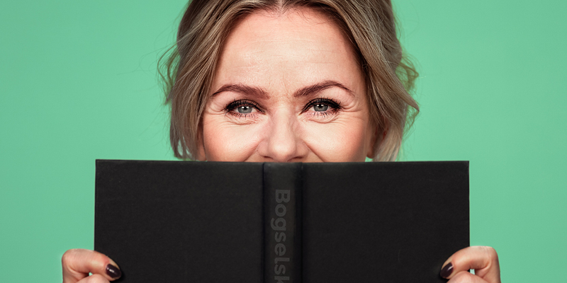 Anne Glad, der holder en opslået bog op foran ansigtet