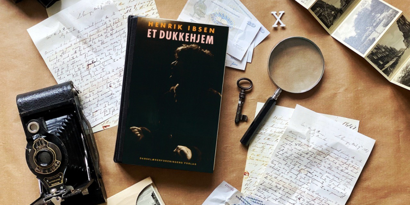 Foto af lup, kikkert, kamera, nøgle, håndskrevne breve, sort/hvide fotos, gamle pengesedler og bogen Et dukkehjem af Henrik Ibsen
